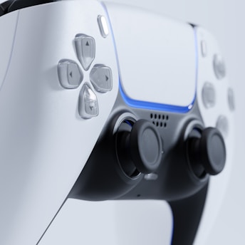 A close-up view of a modern gaming controller, featuring a sleek design with white and black coloration. The image highlights buttons and joysticks, with a blue light accentuating the controller's curves.