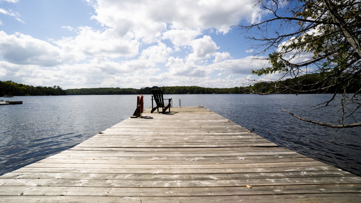 A single chair at the end of a wooden dock on a calm lake
