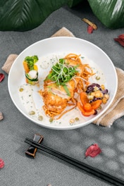 A beautifully plated dish featuring golden crispy ginger chicken with colorful vegetables and a drizzle of sauce on a deep red plate.