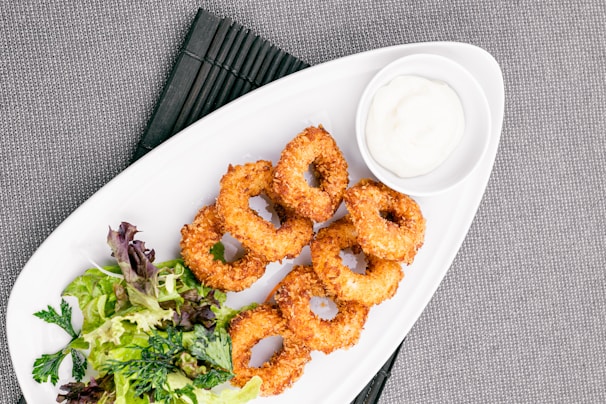 A plate of golden onion rings served with a dipping sauce.