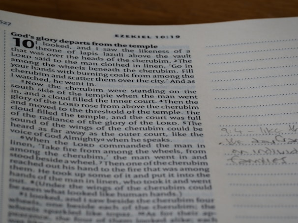 A close-up view of a page from a book with a passage from Ezekiel 10:1-19. The text is black and aligns in justified margins on an off-white background. On the right side, there is a lined margin with some handwritten notes in blue ink.