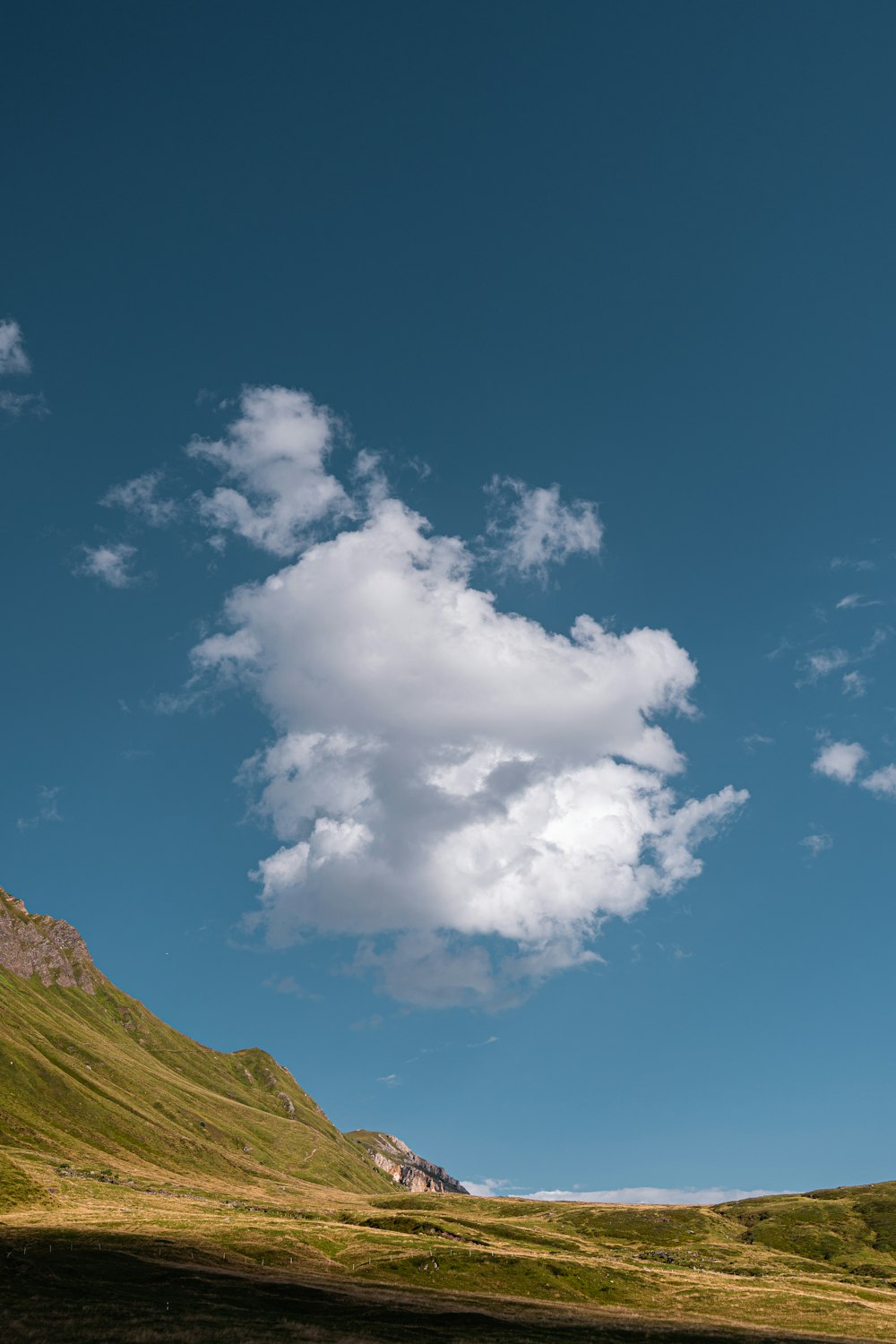 a large cloud is in the sky above a grassy hill