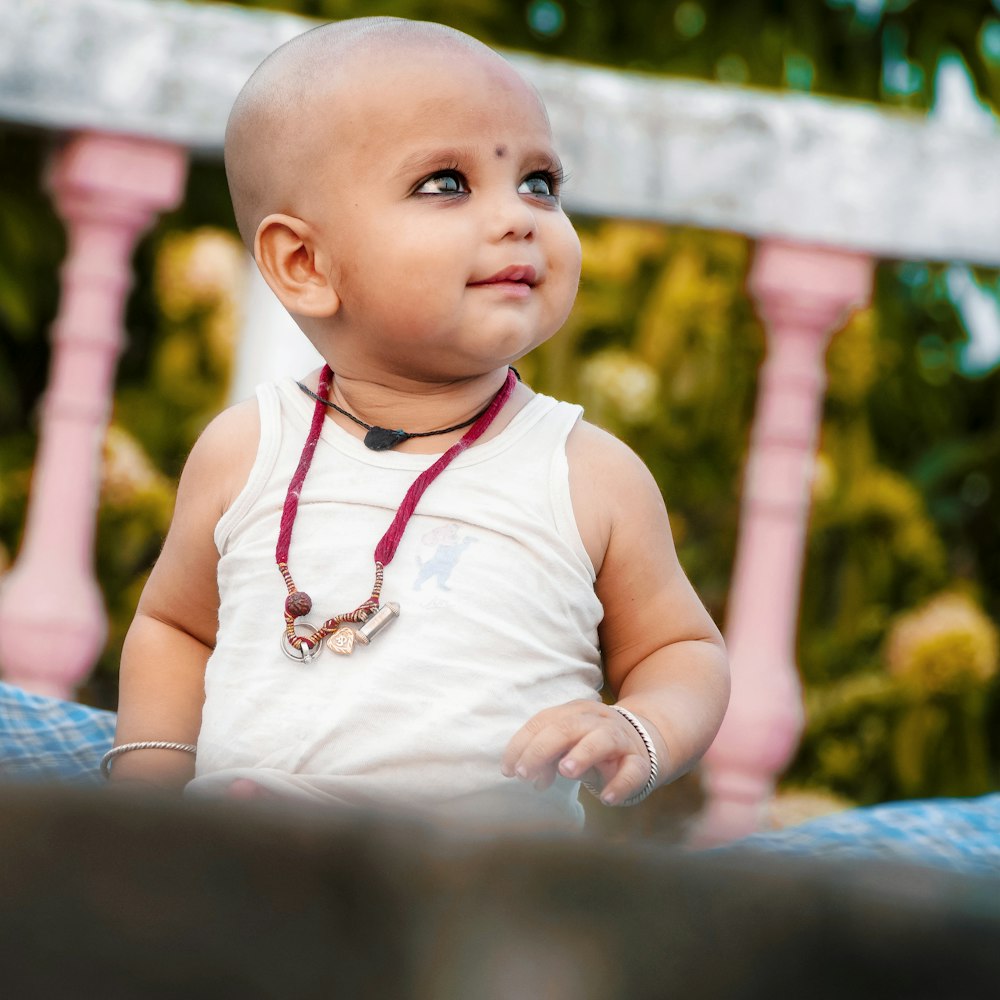 a baby with a necklace on sitting on a blanket