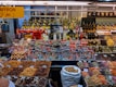 A colorful display at a market stall featuring a variety of packaged goods, spices, nuts, dried fruits, and bottles of oils and spirits. The assortment of products is neatly arranged, with saffron prominently indicated by a yellow sign in both English and Arabic. The well-lit space showcases a vibrant and organized selection, capturing the lively ambiance of a market setting.