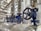 A close-up view of several industrial valves with blue metal bodies and black hand wheels on a series of pipes. The setting appears to be within a mechanical or industrial facility, with stainless steel pipes and fittings.