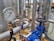 A close-up of an industrial pressure gauge displaying measurements in kilopascals with surrounding metal pipes and blue valve components in a blurred background.