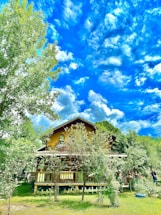 Modern two-story Bali-style house with lush garden and clear blue sky background.
