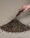A hand is pouring a pile of gravelly soil onto a beige surface. The soil is a mixture of variously sized pebbles and dirt, forming a small mound.