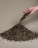 A hand is pouring a pile of gravelly soil onto a beige surface. The soil is a mixture of variously sized pebbles and dirt, forming a small mound.