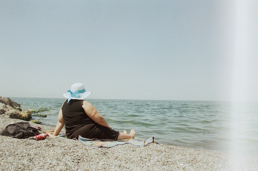 eine frau, die an einem strand neben dem meer sitzt