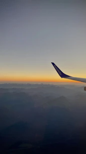 A scenic view of an airplane flying over mountains during sunset.