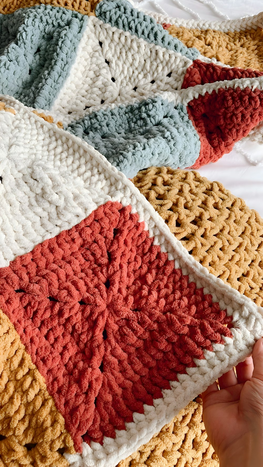 a person holding a crocheted blanket on top of a bed