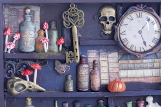 A collection of vintage apothecary bottles, ornate keys, and small red and white mushrooms are arranged on shelves. There is an antiquated clock with Roman numerals, a decorative skull, and a miniature pumpkin nearby, all set against a backdrop of old books.