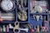 A shelf filled with various curiosities, including a vintage clock with Roman numerals, small decorative skulls, an ornate face mask, and tiny bottles. The shelves are lined with fake books, and there are small mushrooms and bone replicas adding a mystical feel.