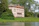A picturesque, classical-style villa with a light peach facade is surrounded by lush greenery. The two-story building features large windows and ornate details. It's nestled among tall trees beside a tranquil body of water.