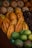A variety of tropical fruits are displayed in close arrangement, including pineapples, cacao pods, and green mangoes. The fruits are layered in rows, showcasing their distinct colors and textures.