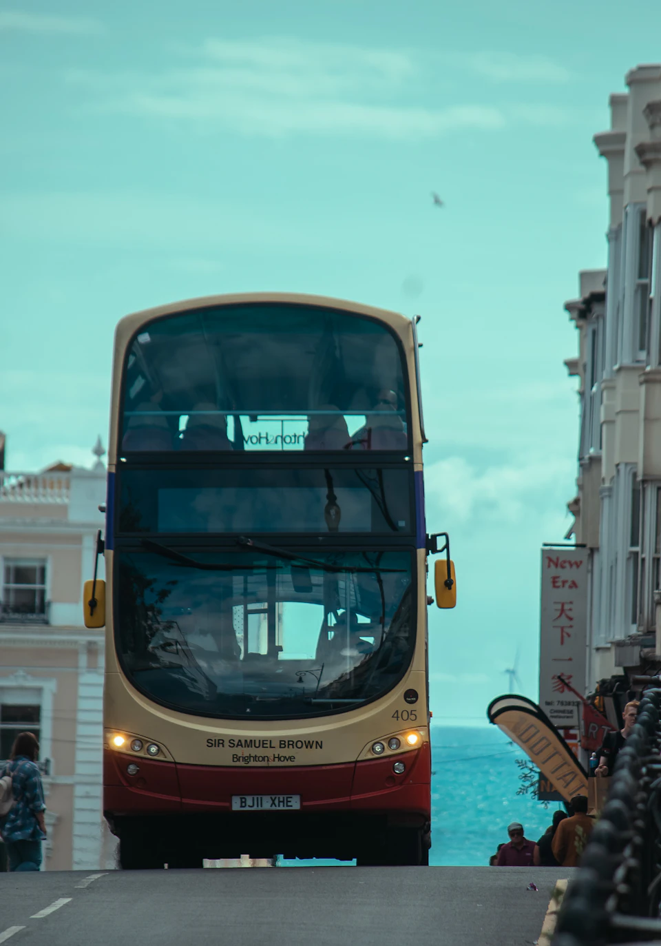 Yellow and red double-decker bus drives down street lined with white buildings and shops
