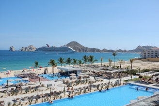 a large swimming pool next to a beach with a cruise ship in the background