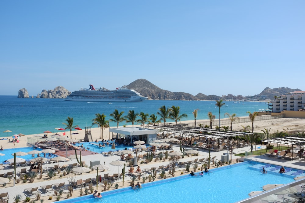 a large swimming pool next to a beach with a cruise ship in the background