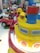 Two children wearing Pikachu-themed outfits sit in a colorful amusement ride surrounded by other vibrant play equipment. The scene is filled with bright colors and playful elements, suggesting a fun and lively environment.