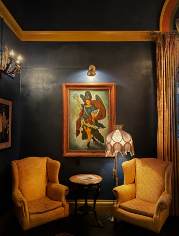 A cozy corner with a framed original landscape painting hanging above a plush chair.