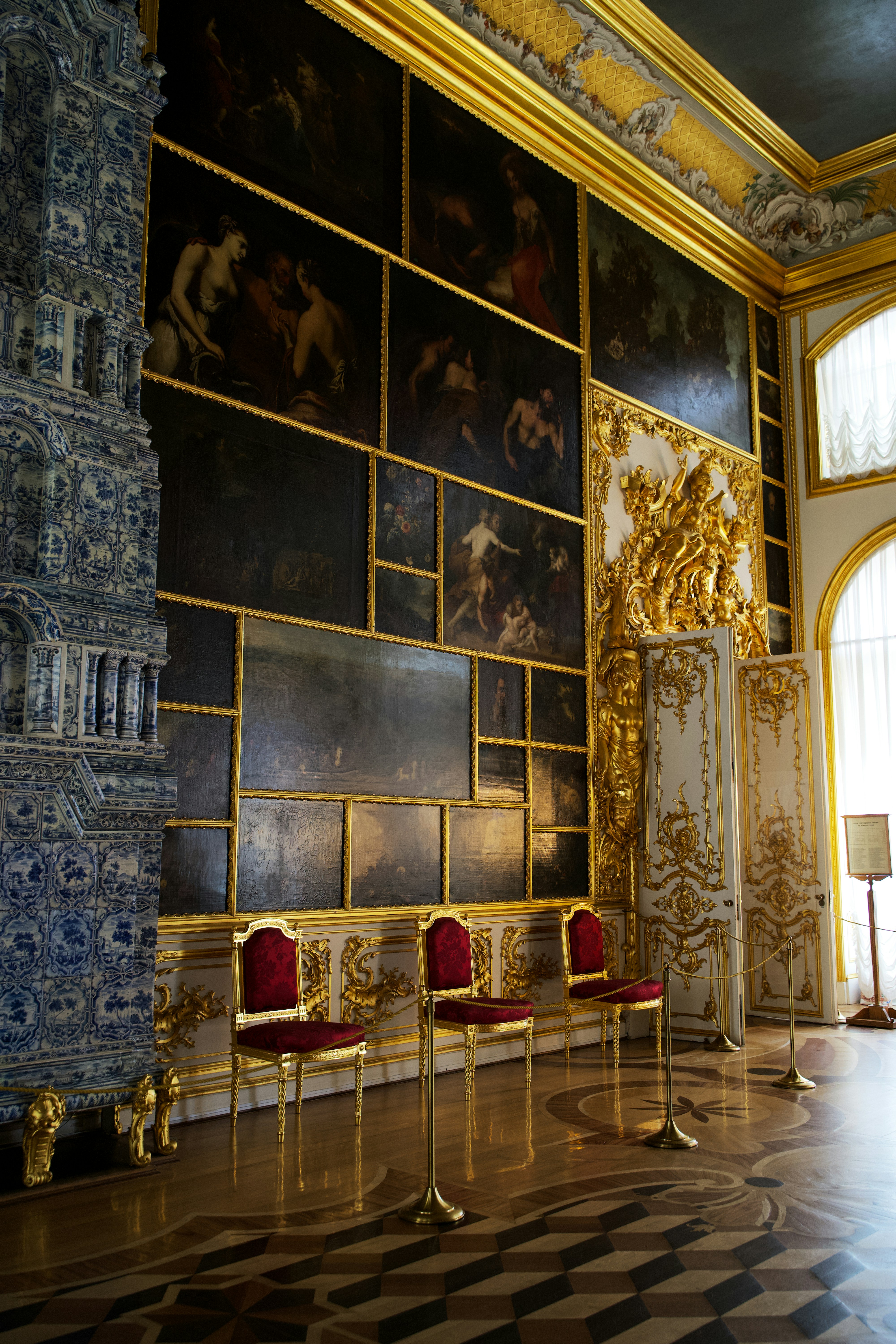 Ornate palace room featuring gold framed paintings and velvet chairs.