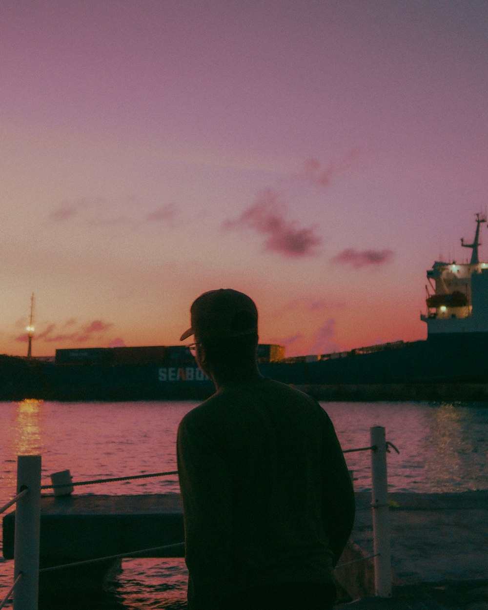 a man standing on a dock watching the sunset