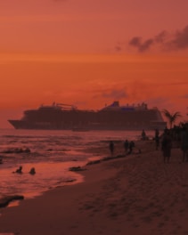 A majestic cruise ship sailing past a tropical island at sunset.