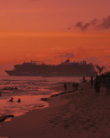 A vibrant cruise ship sailing past a tropical island at sunset.