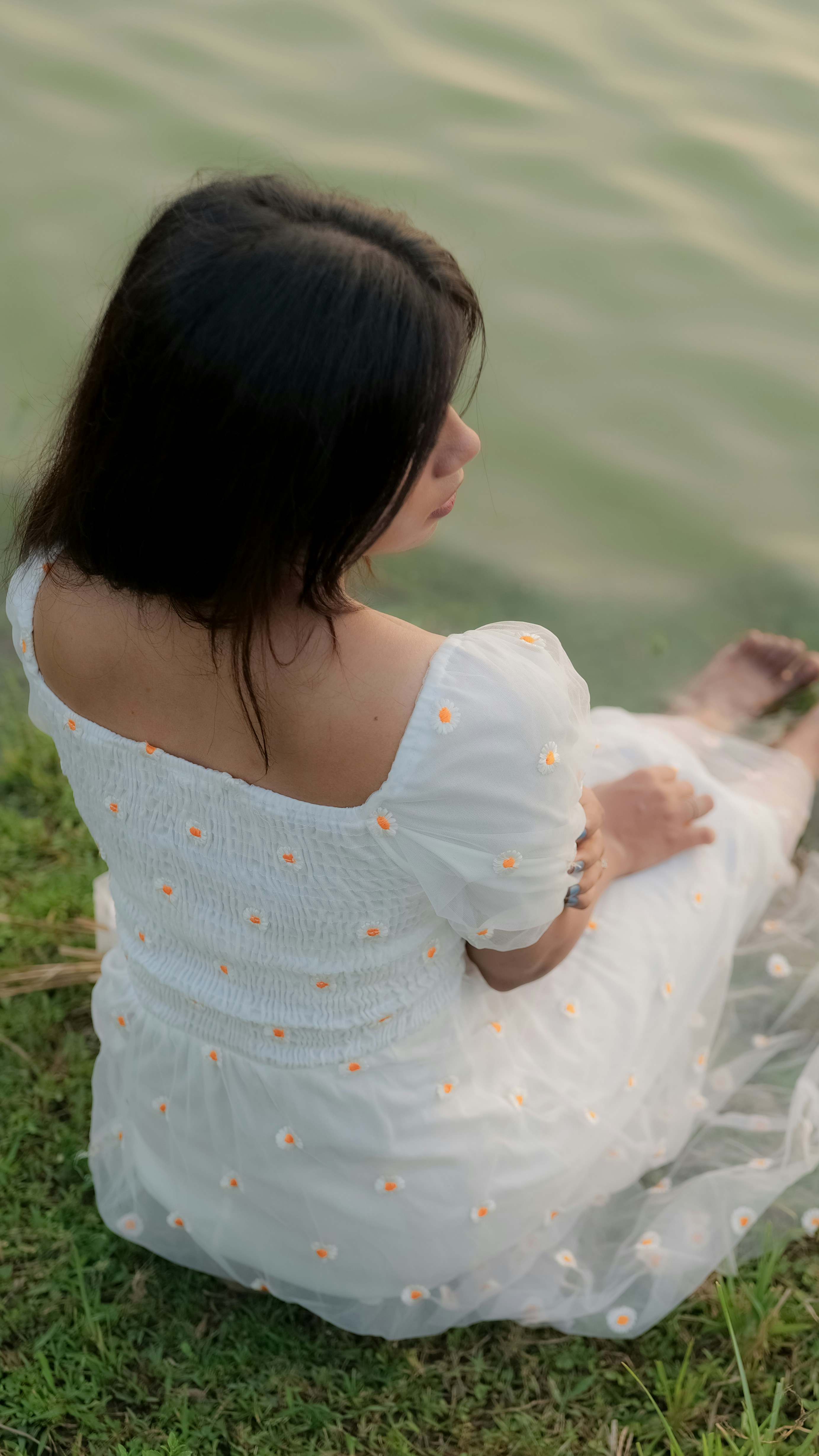 a woman in a white dress sitting by the water