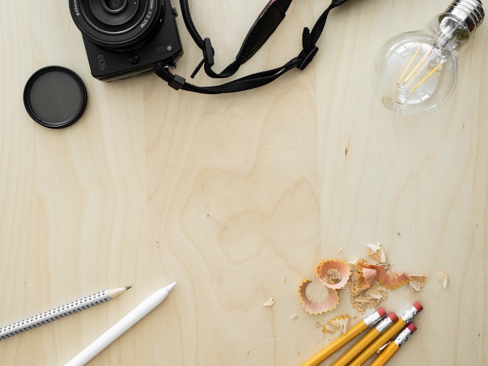 a camera, pencils, a camera lens, and other items on a table