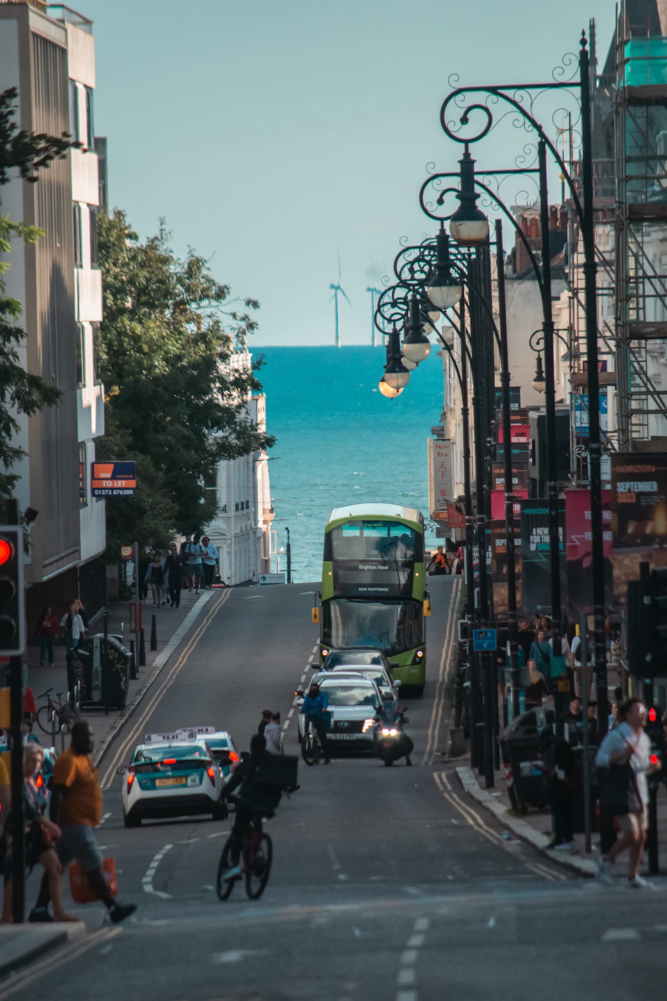 Green double-decker bus drives through crowded city street with pedestrians and various vehicles nearby