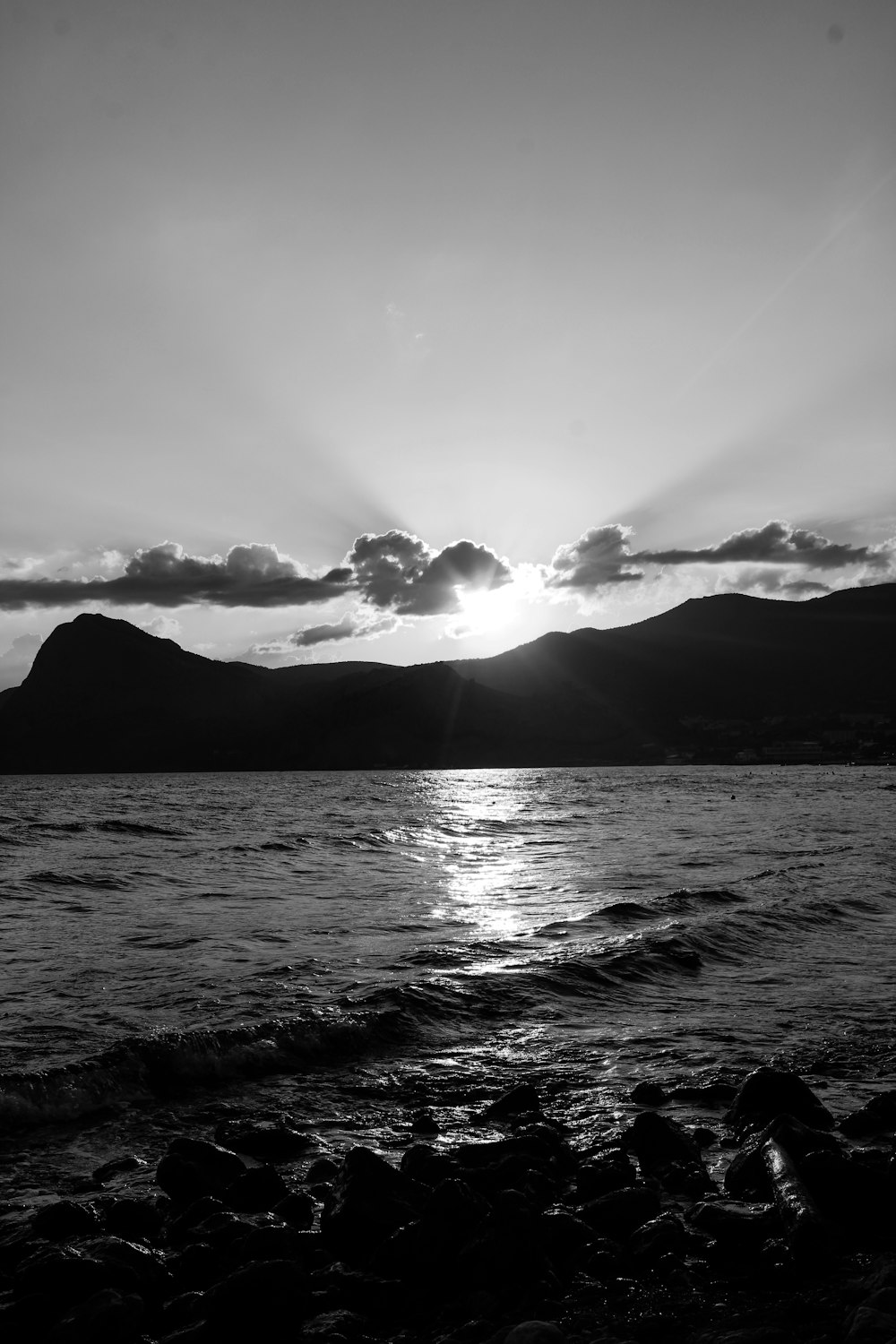 a black and white photo of the sun setting over a body of water