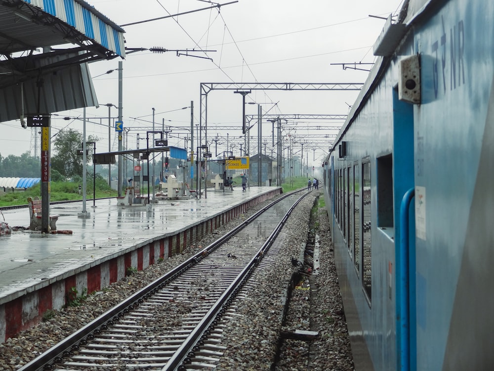 a blue train traveling down train tracks next to a train station