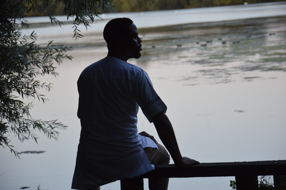 a man sitting on a bench next to a body of water