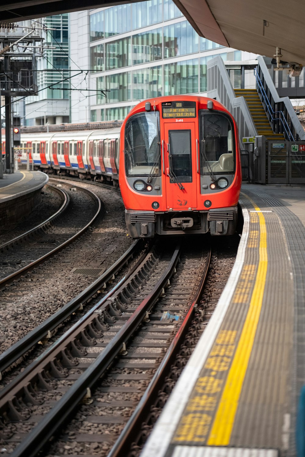 a red train traveling down train tracks next to a tall building