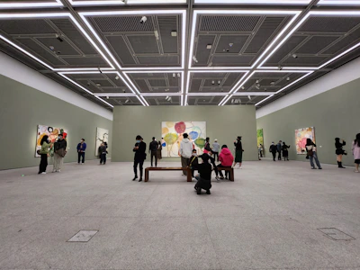 A bright, minimalist art gallery room with golden accents and large oil paintings displayed on white walls.