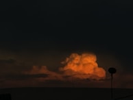 Brightly lit orange clouds are seen in the dark sky, creating a striking contrast. A silhouette of a dish antenna is visible in the foreground, adding an element of human presence to the otherwise natural scene.