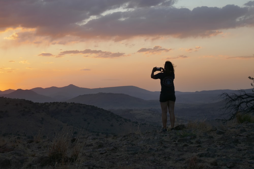 a woman taking a picture of a sunset