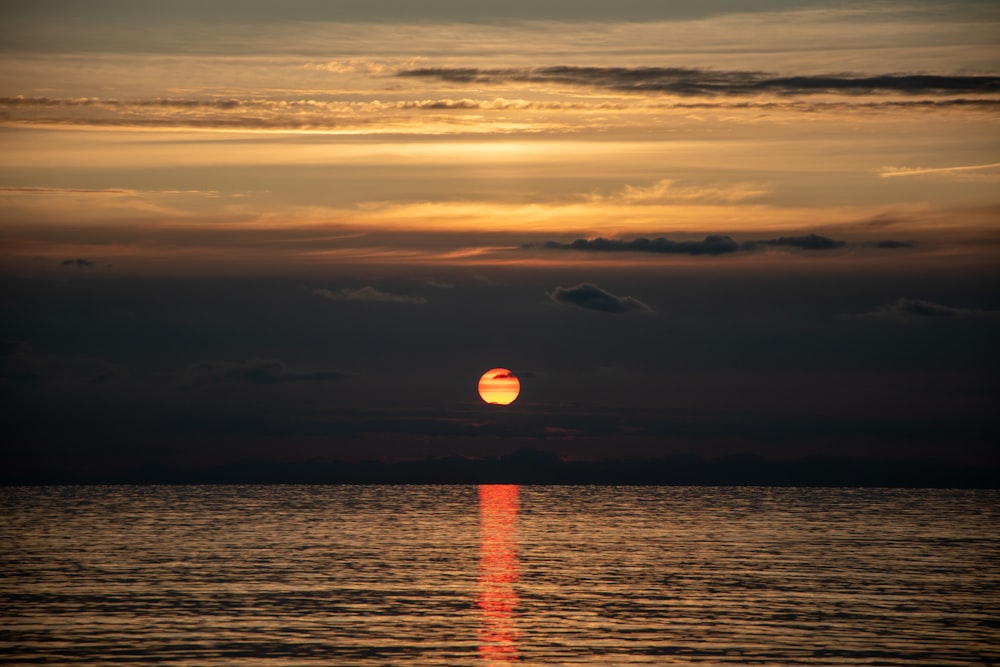 the sun is setting over the ocean on a cloudy day