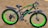 A fat tire electric bike with a sleek black frame and vibrant green accents. The bike stands on sandy ground and features large, thick tires with 'XTRA ACTION' branding on the sidewalls. The seat is cushioned and ergonomic, designed for comfort.