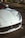 A luxurious white sports car is parked in an urban setting, with distinctive features including sleek lines and a prominent front grille. The car carries a Dubai license plate, and the background suggests a city environment with visible road markings and landscaping.