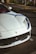A luxurious white sports car is parked in an urban setting, with distinctive features including sleek lines and a prominent front grille. The car carries a Dubai license plate, and the background suggests a city environment with visible road markings and landscaping.