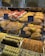 A display of various baked goods in a bakery. There are pastries topped with fresh strawberries, flaky danishes with custard, and assorted cookies with chocolate and pistachio. The shelves are filled with different types of breads and sweets, each labeled with small signs.