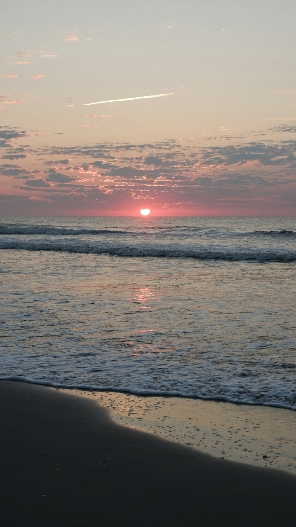 the sun is setting over the water at the beach