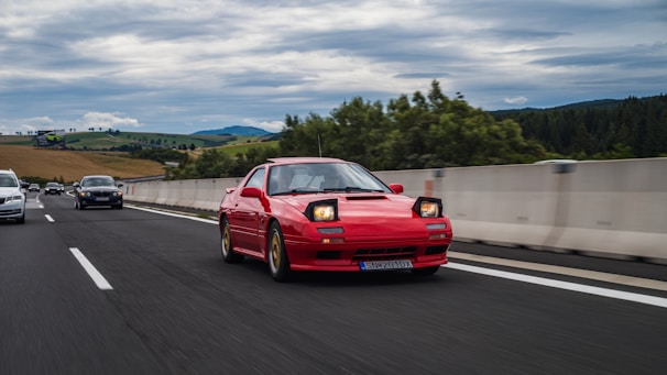 Dynamic shot of a red sports car speeding along a coastal highway under a cloudy sky