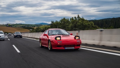 A red Audi cruising along a scenic highway with hills in the background.