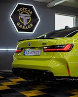A vibrant green sports car is positioned inside a modern garage. The sleek design is highlighted by the bright red taillights. A sign reading 'TopCar Garage' is illuminated in the background with contrasting neon lights. The car is parked on a black and yellow checkered floor, enhancing the bold aesthetic.