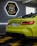 A vibrant green sports car is positioned inside a modern garage. The sleek design is highlighted by the bright red taillights. A sign reading 'TopCar Garage' is illuminated in the background with contrasting neon lights. The car is parked on a black and yellow checkered floor, enhancing the bold aesthetic.