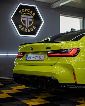 A vibrant green sports car is positioned inside a modern garage. The sleek design is highlighted by the bright red taillights. A sign reading 'TopCar Garage' is illuminated in the background with contrasting neon lights. The car is parked on a black and yellow checkered floor, enhancing the bold aesthetic.